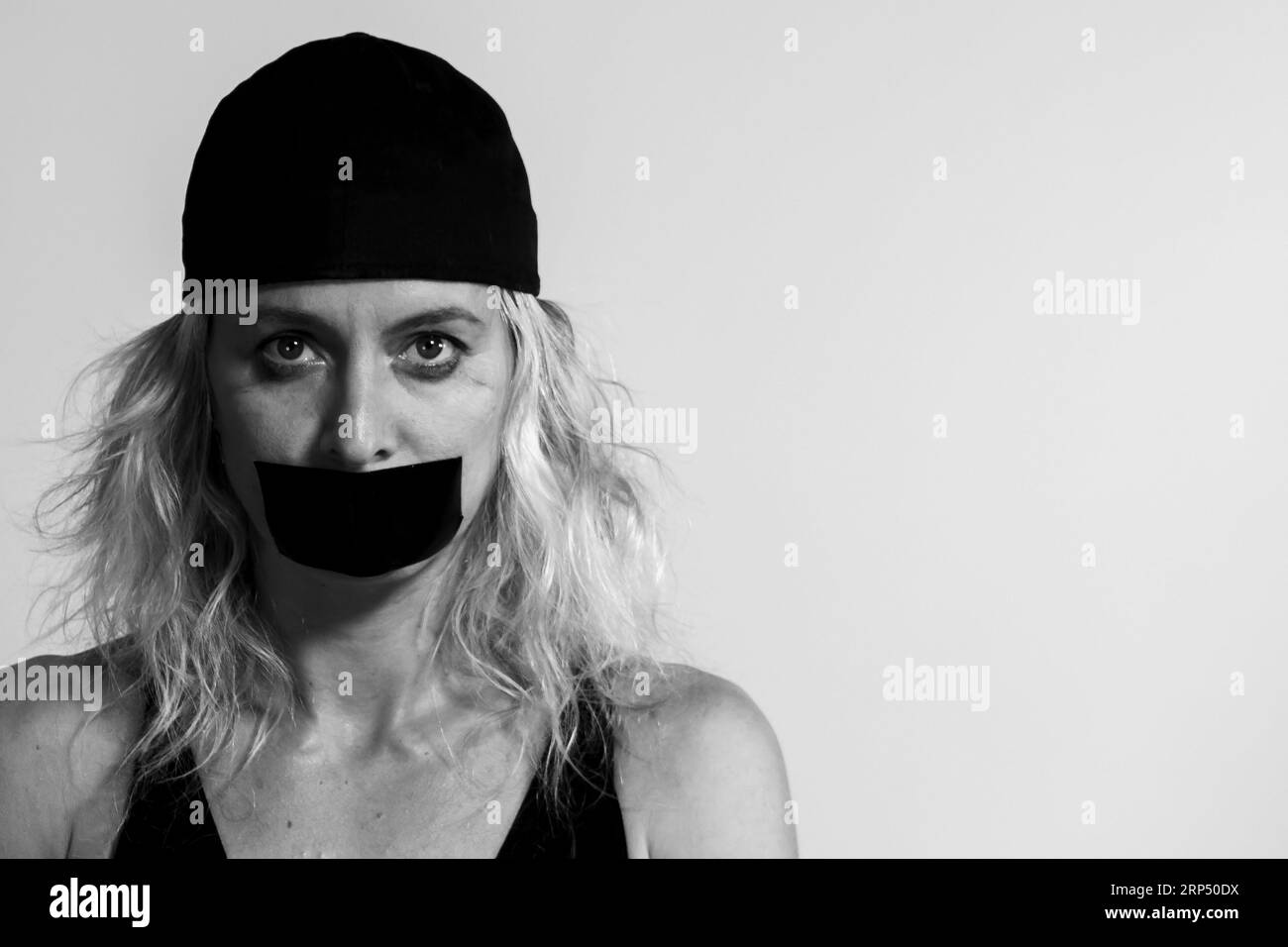 Light-eyed blonde woman with a cap and her mouth taped so she can't speak Stock Photo