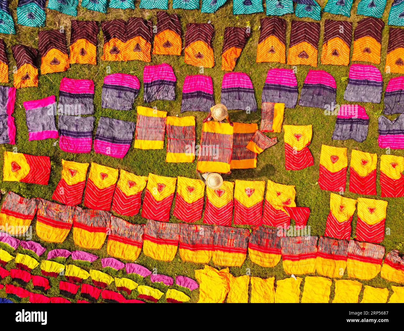 Narayanganj, Bangladesh. 3rd Sep, 2023. Hundreds of pieces of dyed cloth are spread out across a field at Batik Village for drying, which looks like a Kingdom of Colors. Workers use hats for protection from the scorching heat because they have to constantly turn the colorful fabrics so that they dry perfectly in the sunlight. Beautifully embellished colorful cloths are created using the Indonesian technique called ''Batik''. Parts of the design are blocked out by applying hot wax over them, then a dye is applied on top and the parts covered in wax resist the dye and remain the original col Stock Photo