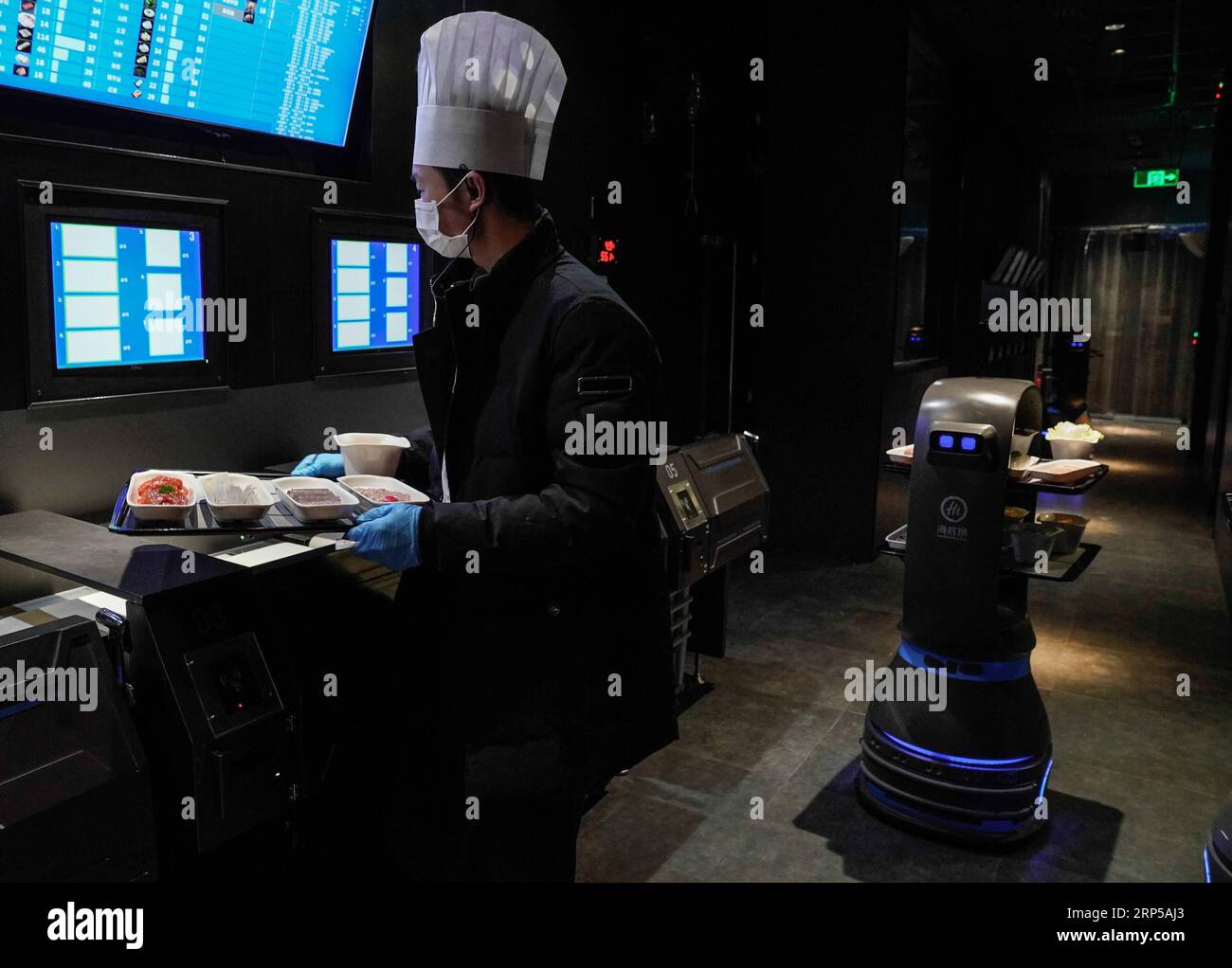 (181206) -- BEIJING, Dec. 6, 2018 -- A delivery robot and a waiter work at the kitchen of a hot pot restaurant in Beijing, capital of China, Dec. 5, 2018. A hot pot restaurant which integrates artificial intelligence, big data management and smart robot service has attracted lots of consumers. After customers order their dishes with a tablet computer, robotic arms in the kitchen get all dishes ready and then the delivery robots sent the dishes to the tables. Workers in the kitchen control all the procedures and also monitor the data for better management. ) (zwx) CHINA-BEIJING-AI RESTAURANT (C Stock Photo