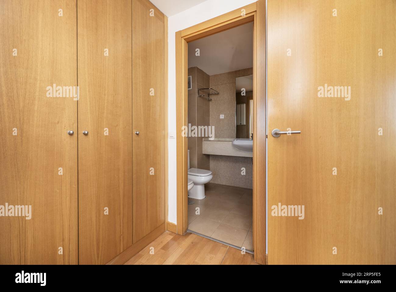 A room with a dressing room with oak doors and access to an en-suite bathroom with white toilets Stock Photo