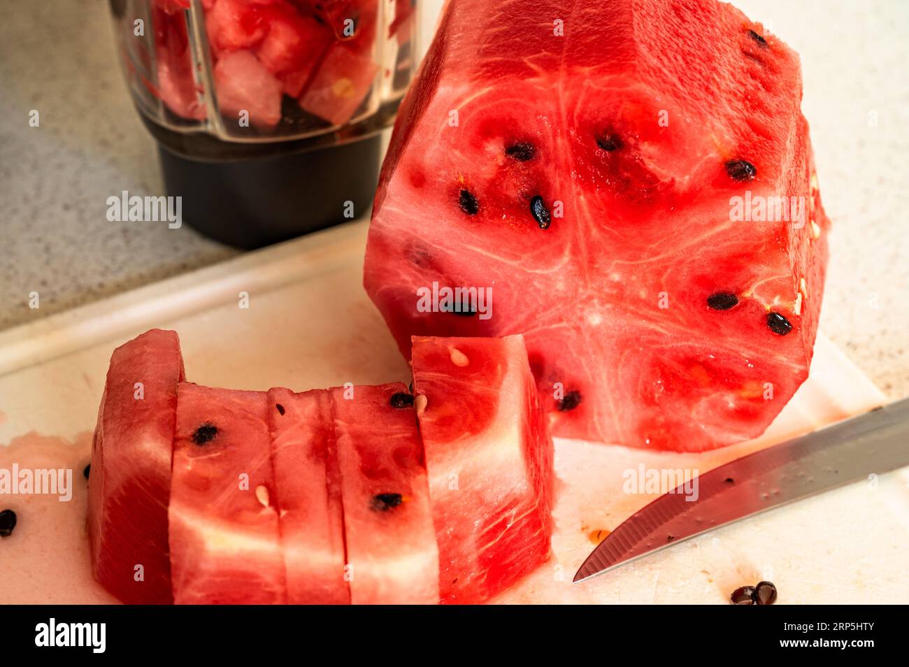 Sliced watermelon, knife and part of mixer on kitchen board, closeup. Stock Photo