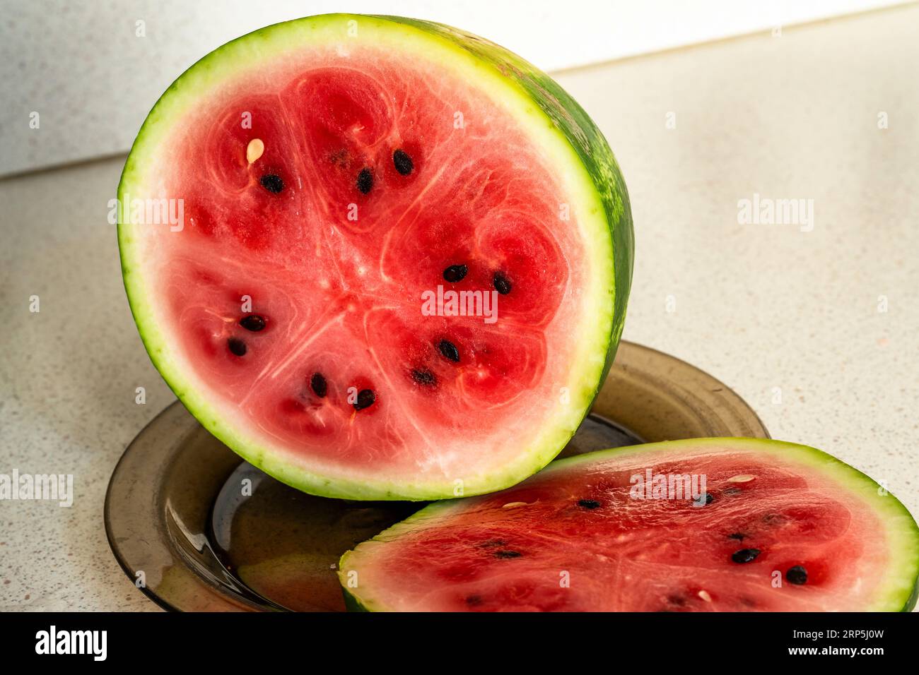Two piece of watermelon on brown plate on beige table. Stock Photo