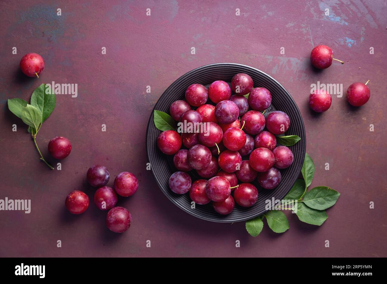 Red sweet cherry plums on black plate. Stock Photo