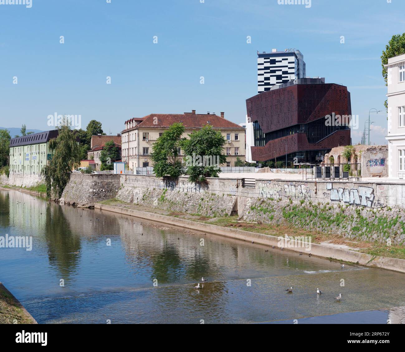 Mixture of old and modern buildings with unusual shapes along the River Miljacks in the city of Sarajevo, Bosnia and Herzegovina, September 03, 2023 Stock Photo