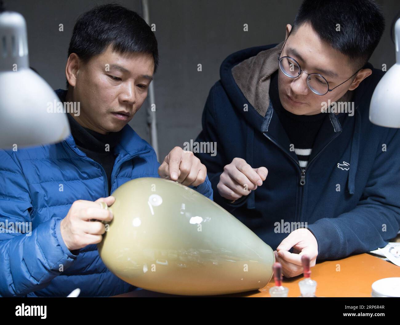 (190119) -- LONGQUAN, Jan. 19, 2019 (Xinhua) -- Wu Rongqiang (L) discusses the repair details with a celadon artist at his studio in Niutouling Village, Longquan City of east China s Zhejiang Province, Jan. 15, 2019. Wu Rongqiang, a Longquan native aged 45, started exploring traditional lacquer art since 2012. In 2017, he moved his family to an old house deep in the mountains in Longquan in order to do more experiments in lacquer undisturbed. He uses lacquer to repair broken porcelain and to create lacquerware. Also, he experiments on the production of various lacquers. I feel so pleased to re Stock Photo