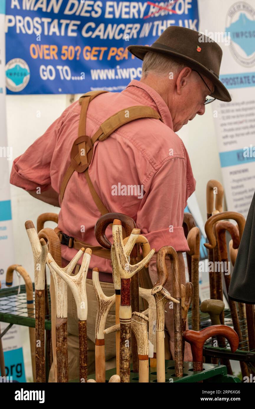 older man making and selling traditional country walking sticks at a craft fair on the isle of wight. Stock Photo
