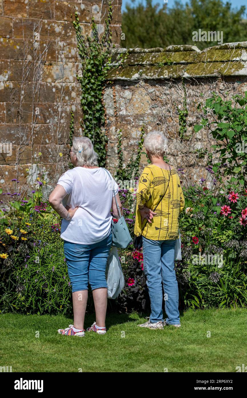 two older retired ladies sharing time together visiting as country house garden on the isle of wight uk. women looking at beautiful manor house garden Stock Photo