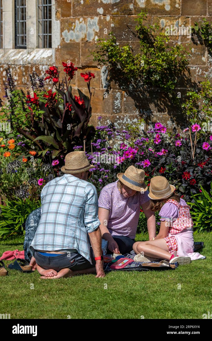 family sitting on a lawn at a country house garden together having a picnic on a summers day. Stock Photo