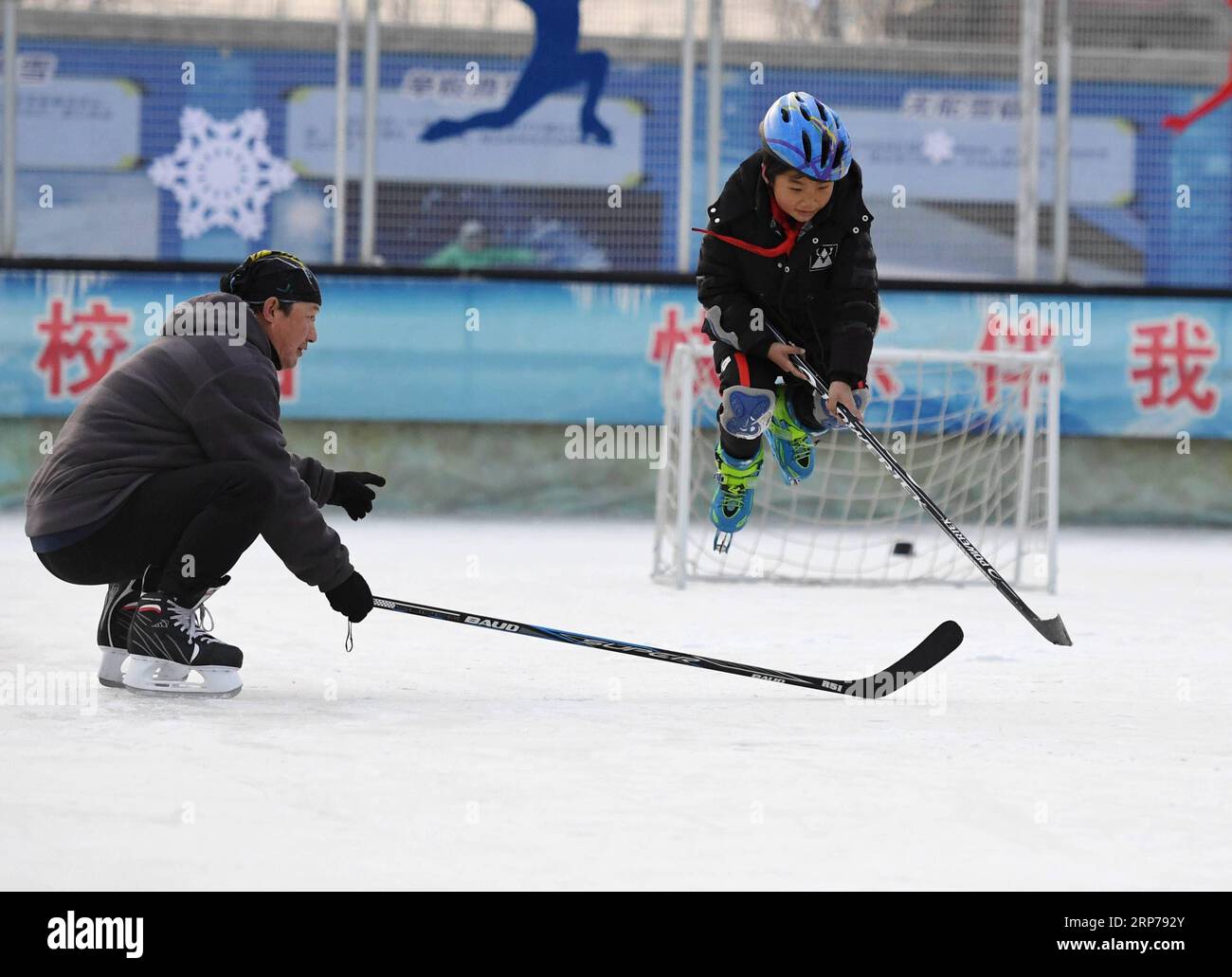 (190201) -- BEIJING, Feb. 1, 2019 (Xinhua) -- Photo taken on Jan. 9, 2019 shows coach Li Chunyu (L) and his student during an ice hockey training session at Taipingzhuang Central Primary School, in Yanqing District of Beijing, capital of China. Taipingzhuang Central Primary School situated right at the foot of Xiaohaituo Mountains, where the venues for Beijing 2022 Winter Olympic games are under construction. Teachers of Taipingzhuang Central Primary School have turned an experimental farmland into a seasonal skating rink for the pupils here to learn skating since 2016. The school hired a expe Stock Photo