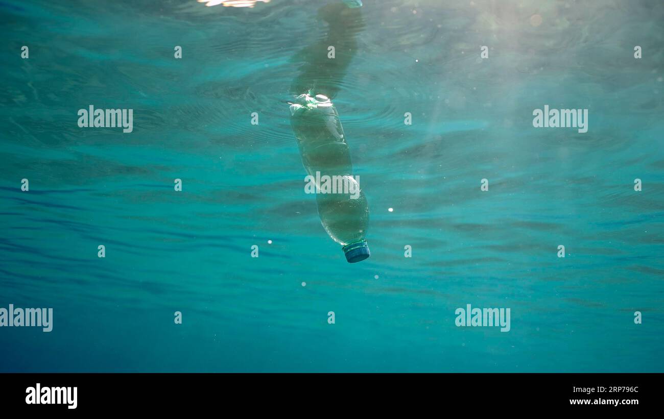 Green plastic bottle drifting under surface of blue water. Plastic pollution of Ocean, Discarded