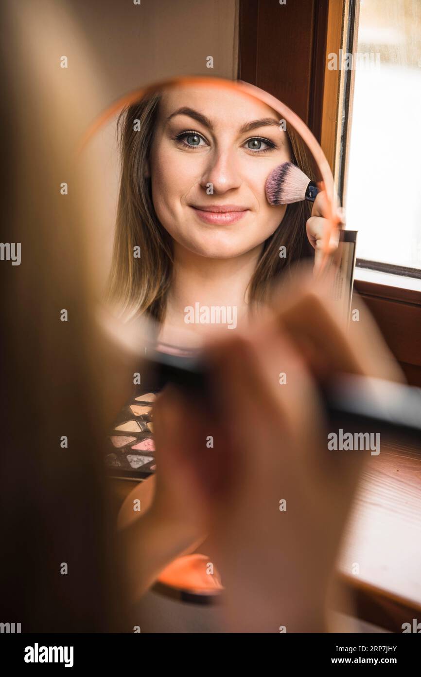 Reflection smiling woman applying blusher her face Stock Photo