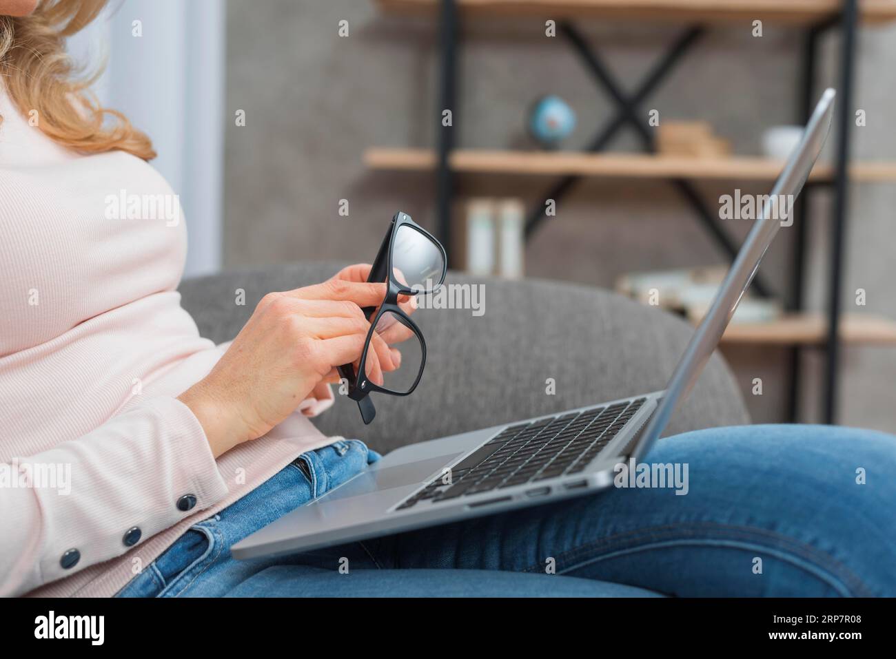 Woman holding eyeglasses hand sitting sofa with open laptop her lap Stock Photo
