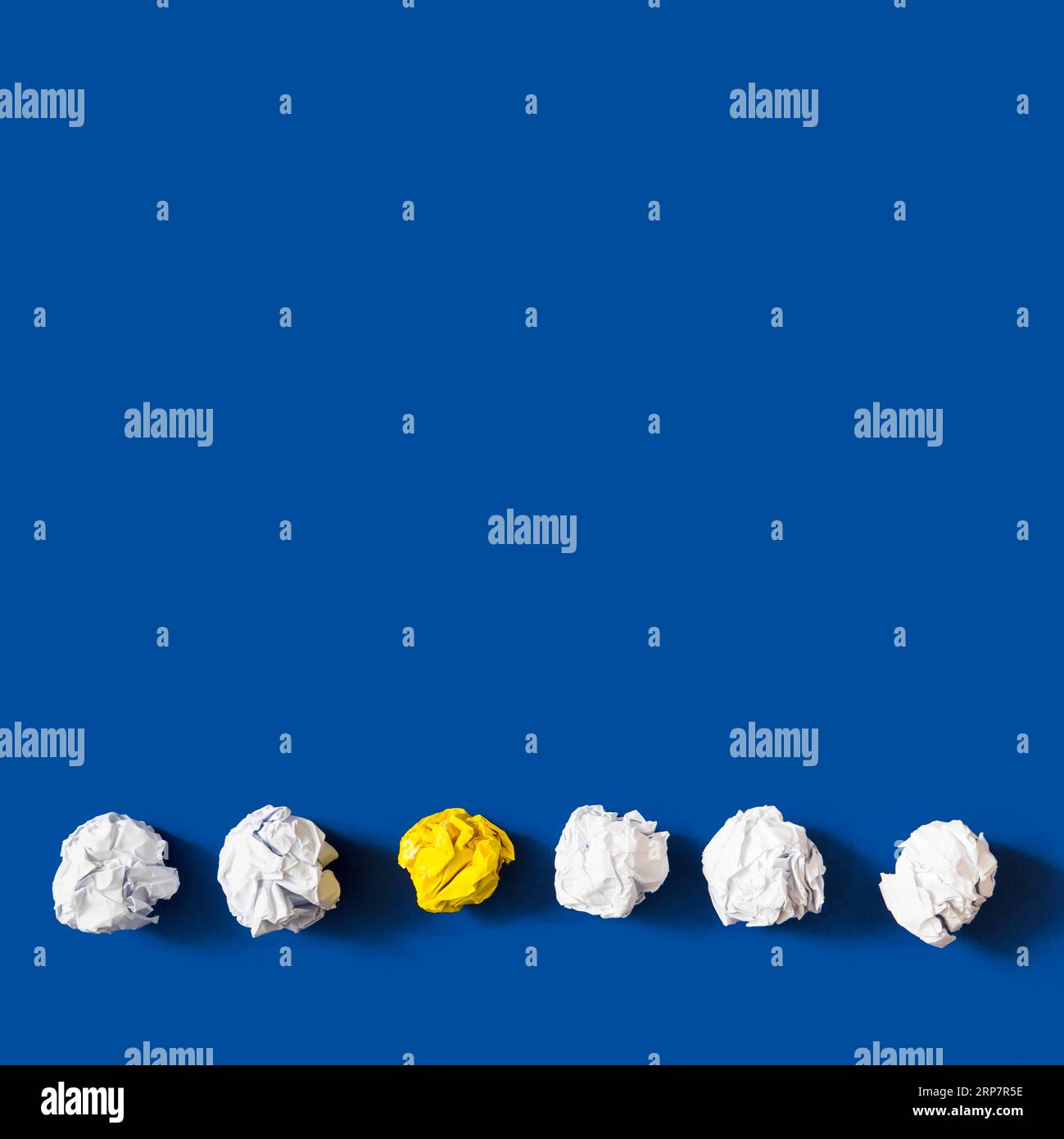 Yellow crumpled paper ball among white balls against blue background