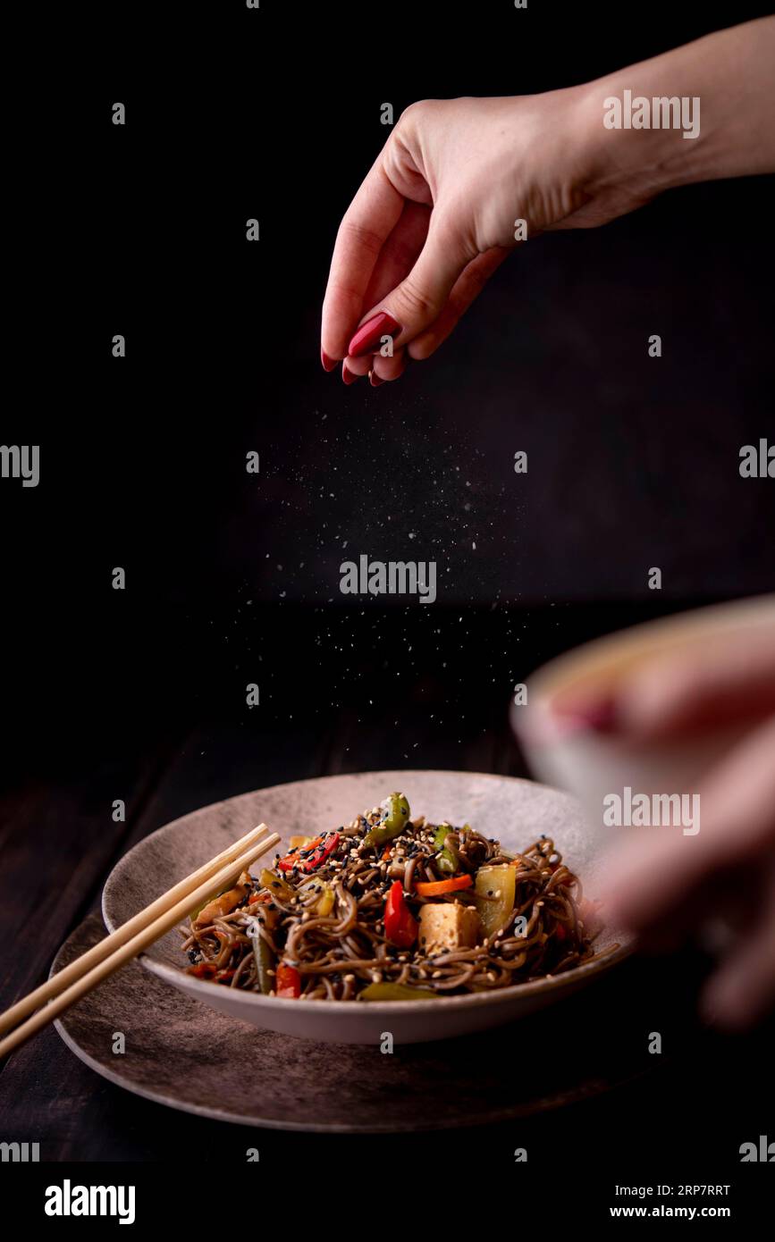 https://c8.alamy.com/comp/2RP7RRT/hand-sprinkling-salt-bowl-noodles-with-vegetables-2RP7RRT.jpg