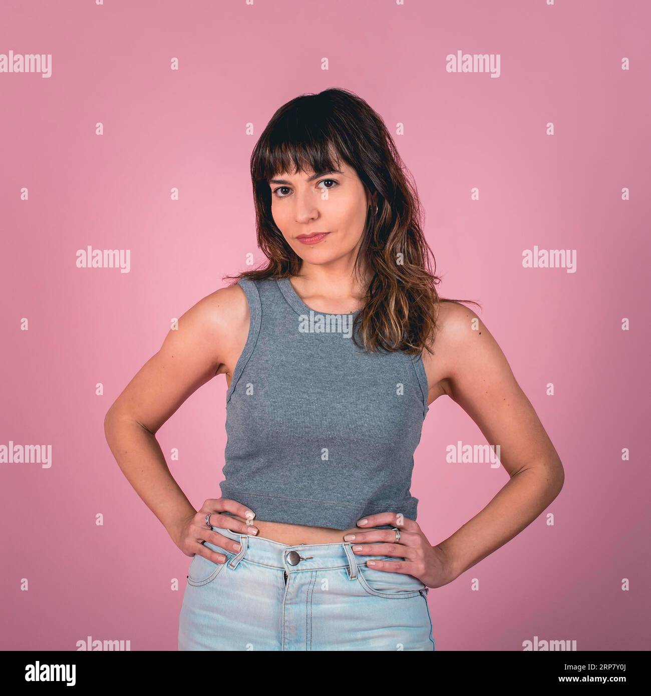 Studio portrait of a confidence woman with hands on hips while looking at camera over a pink background Stock Photo
