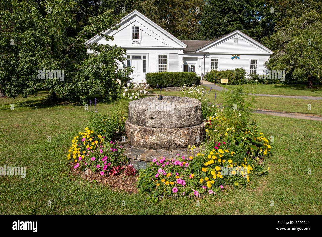 Flowers around stone mill wheels are in front of the Town Library in Warwick, MSA Stock Photo
