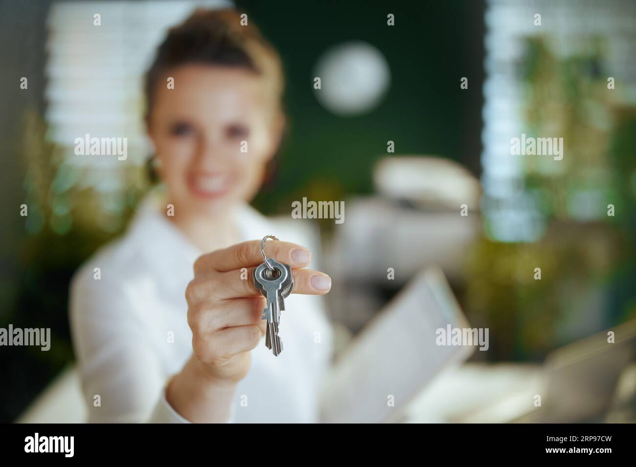 Time to move on. Closeup on modern 40 years old woman realtor in modern green office in white blouse with keys. Stock Photo