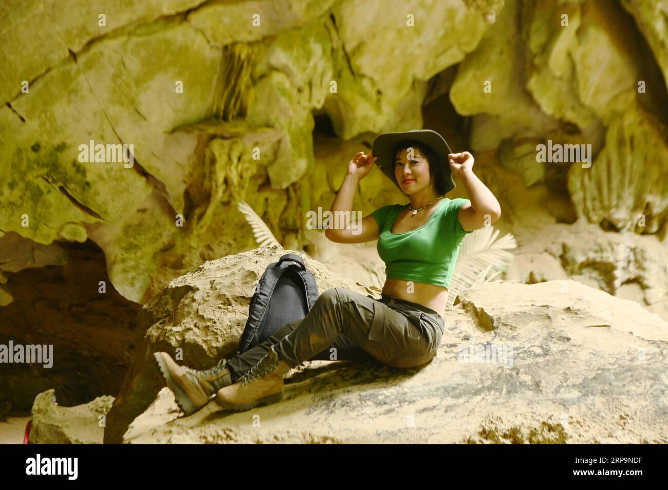 Pretty Asian woman sitting on a rock with happiness and cheerfulness at Tham Hup Pa Tat and is a popular tourist attraction for Thai tourists. Stock Photo