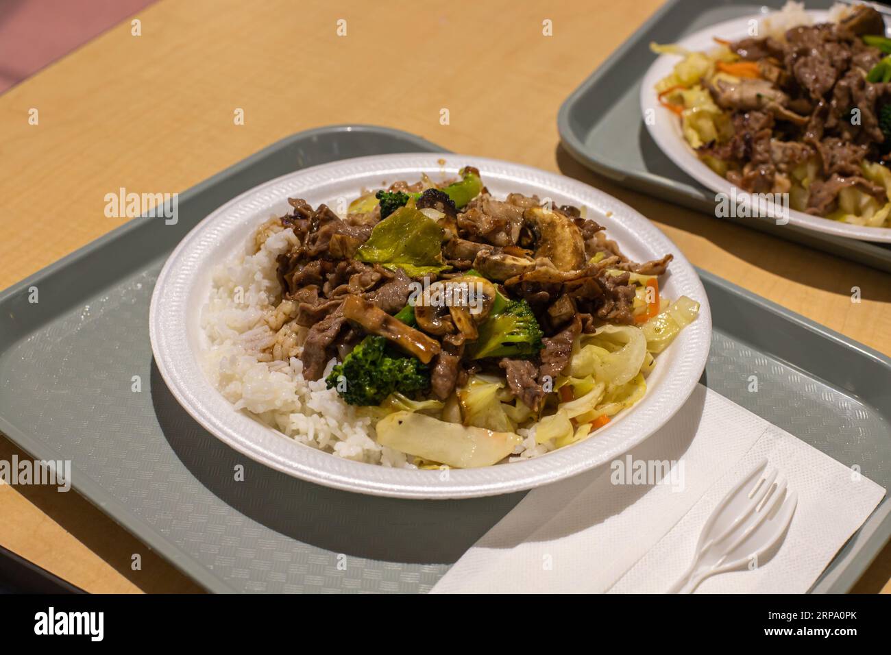 Teriyaki beef and stir-fried vegetables with rice. The dish is at a table in the food court. Stock Photo