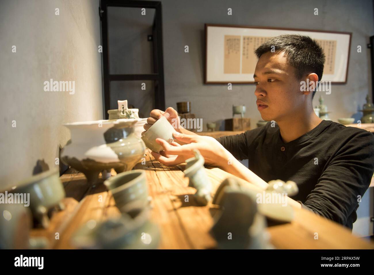 (190520) -- LONGQUAN, May 20, 2019 (Xinhua) -- Lin Song checks his collection of classical Longquan celadon wares at his studio in Longquan, east China s Zhejiang Province, May 20, 2019. Born in 1993, Lin Song is a native of Longquan, home to China s best celadon wares. He received professional training in both his hometown and Jingdezhen, another important porcelain hub of China. Lin had also followed other celadon artisans for years before setting up a studio back home in 2014, focusing on the replication of classical celadon incense burners. Lin s personal collection has grown to over 40 ce Stock Photo