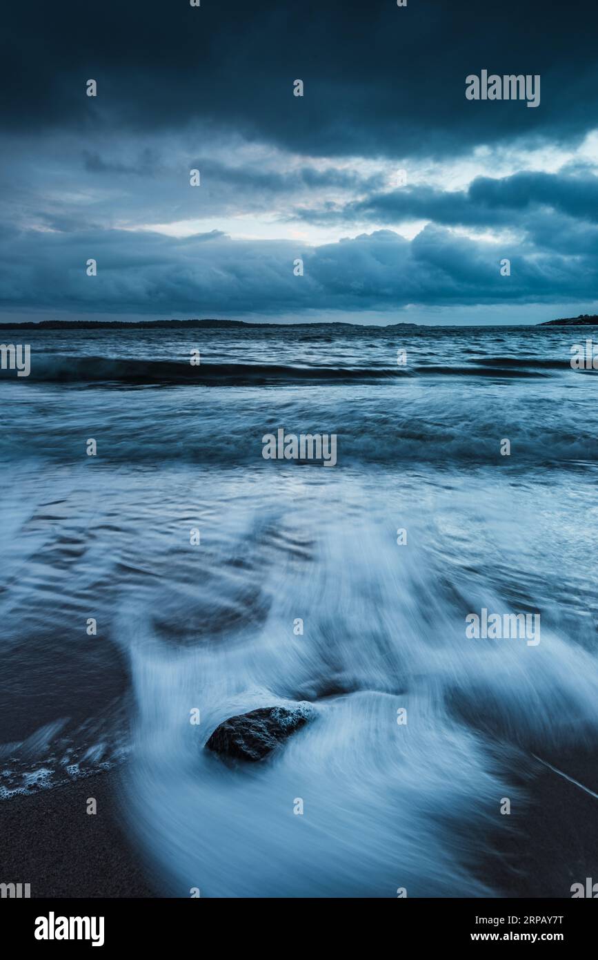 Serenity on a Swedish beach: waves, rocks, cloud-filled sky, and endless ocean horizon. Stock Photo