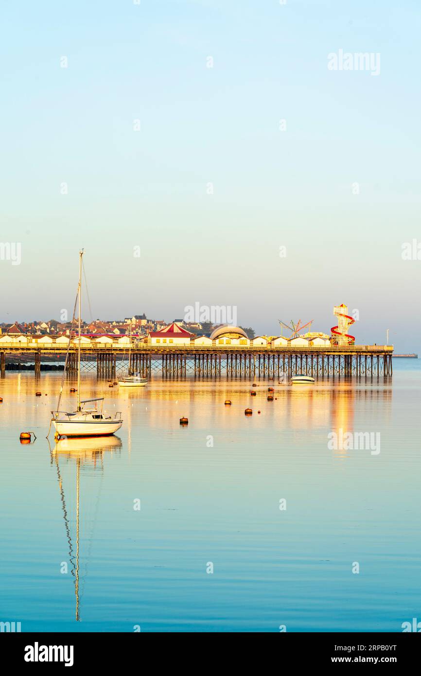 Herne Bay harbour in the soft early light of dawn with the unseen sunrise providing direction lighting. One small yacht moored in the middle of the harbour. Very tranquil and peaceful atmosphere. Stock Photo