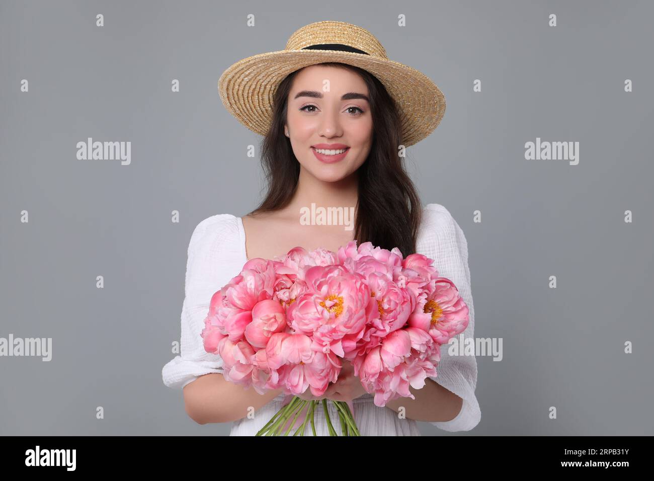 Beautiful young woman in straw hat with bouquet of pink peonies against ...