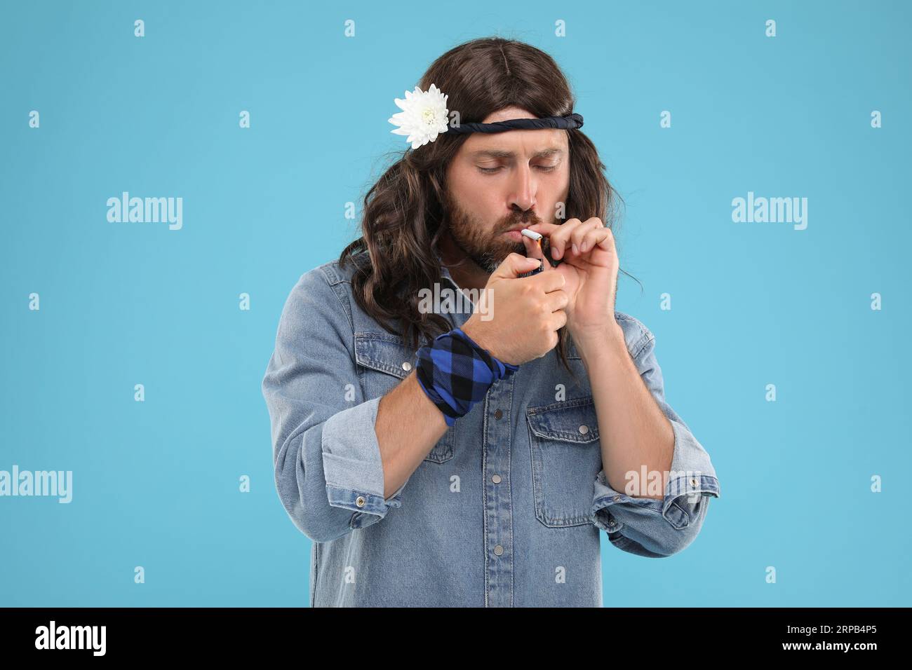 Stylish hippie man lighting cigarette on light blue background Stock Photo