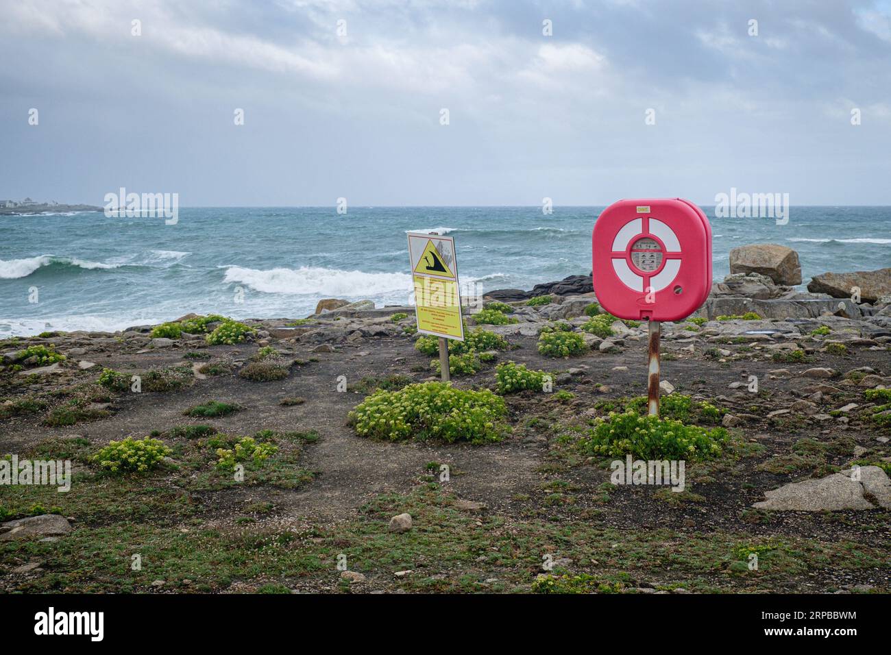 A lifebuoy and a sign informing of mortal danger and swimming prohibited on the Brittany coast with the ocean and waves in the background Stock Photo