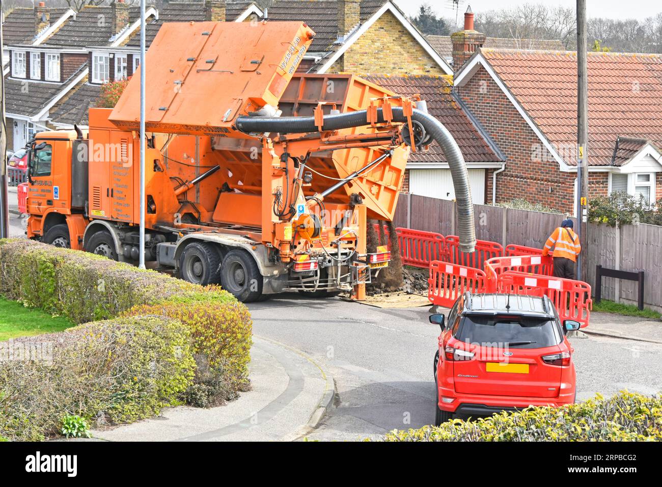 Motorist waits & watches lift tip & empty full storage bin of earth from suction excavation machine on hgv lorry truck into temporary dump compound UK Stock Photo