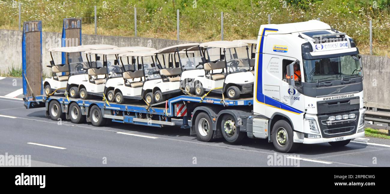 Volvo hgv tractor unit truck and dutch built Nooteboom low loader semi trailer load of Ezgo golf buggies driving along M25 motorway road England UK Stock Photo