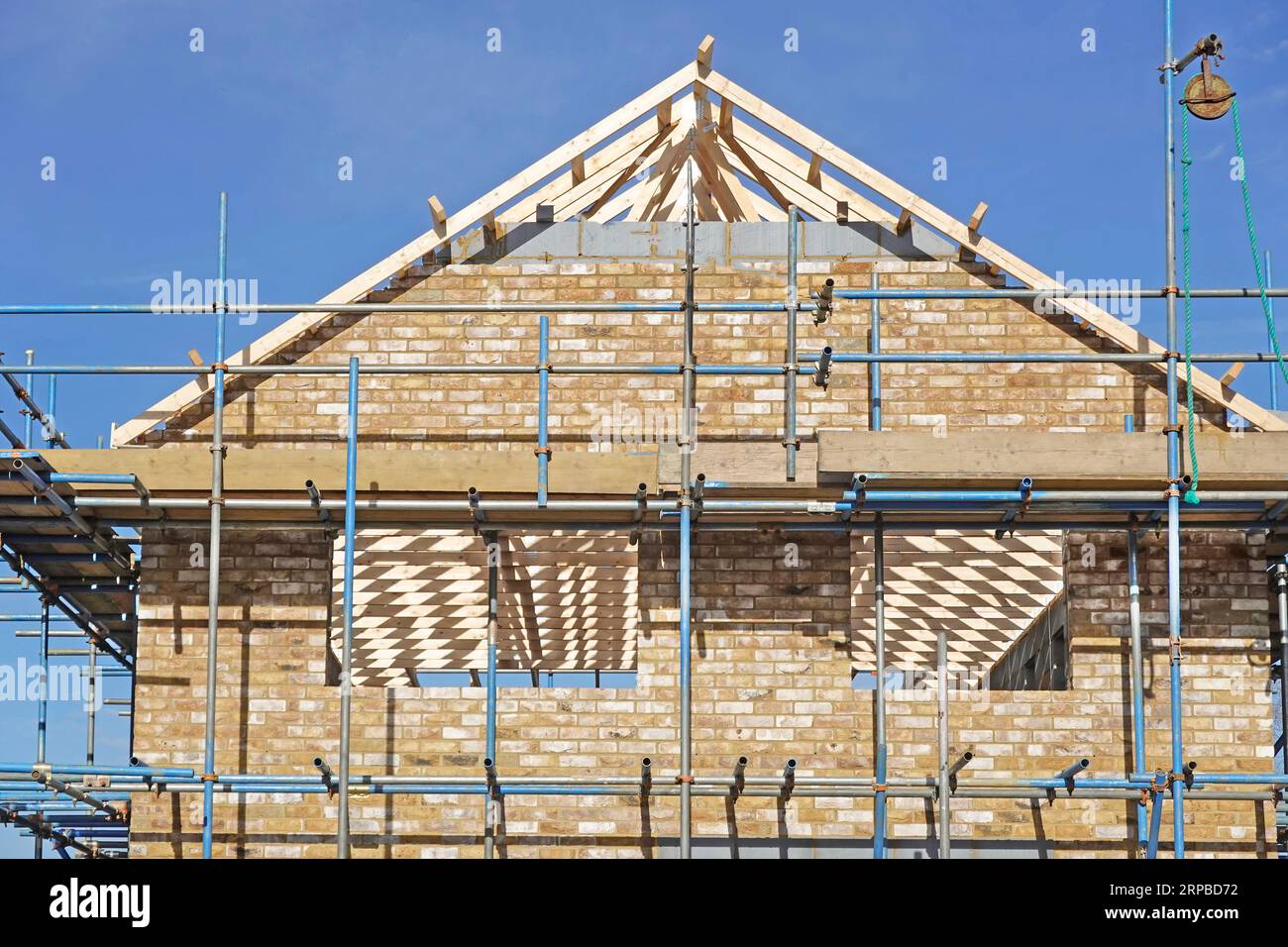 Close up of brick cavity gable end wall & roof in progress from access scaffold prefabricated timber trusses seen through window openings England UK Stock Photo