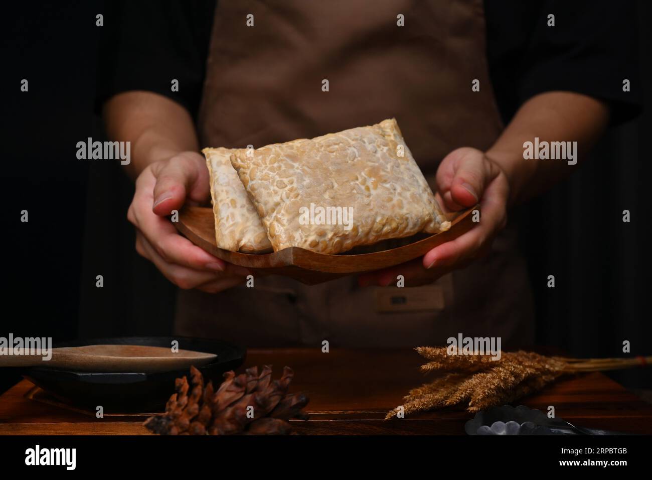 Man wearing apron holding wooden plate with homemade tempeh, healthiest