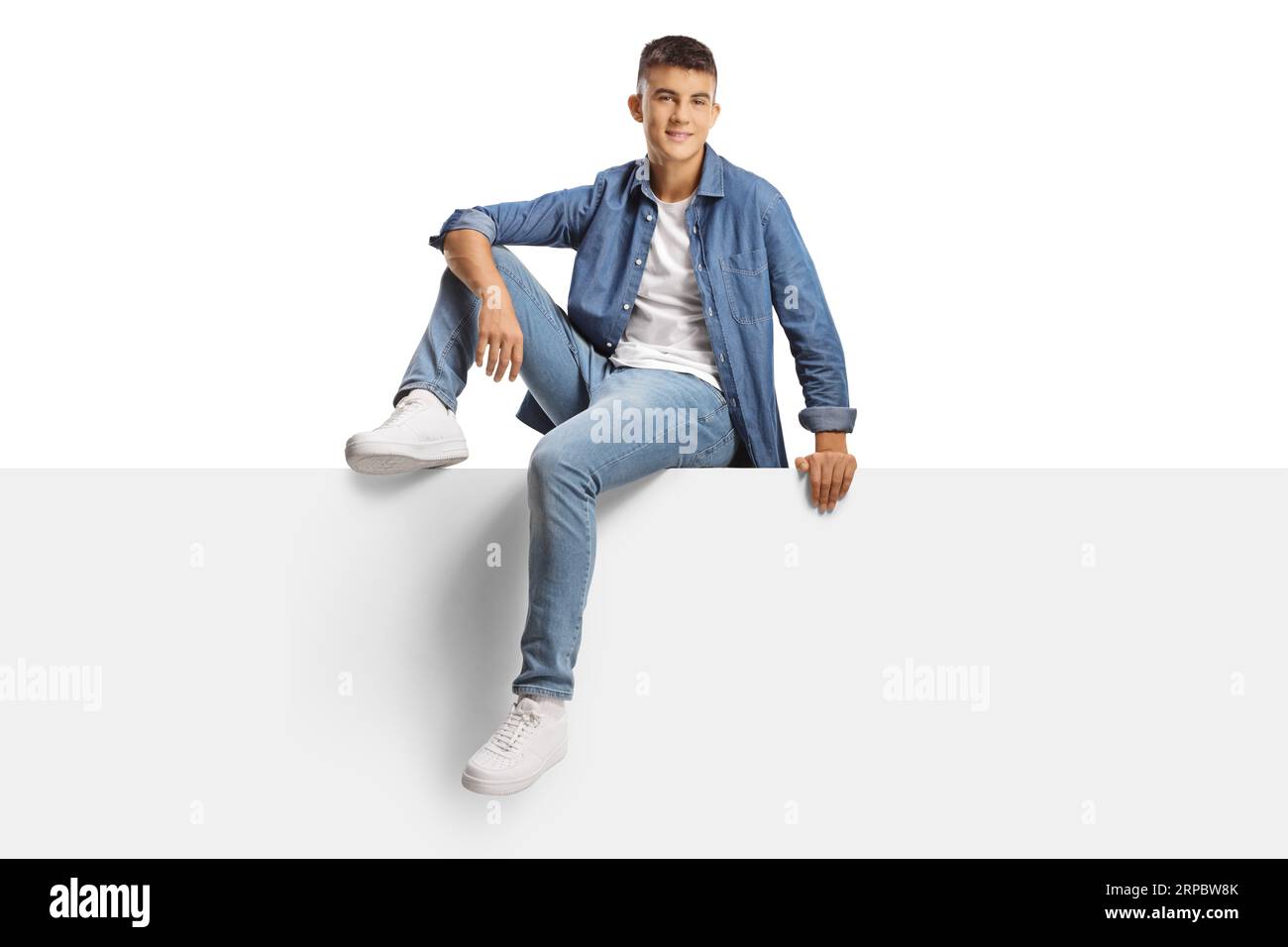 Handsome casual generation z guy sitting on a blank panel isolated on white background Stock Photo