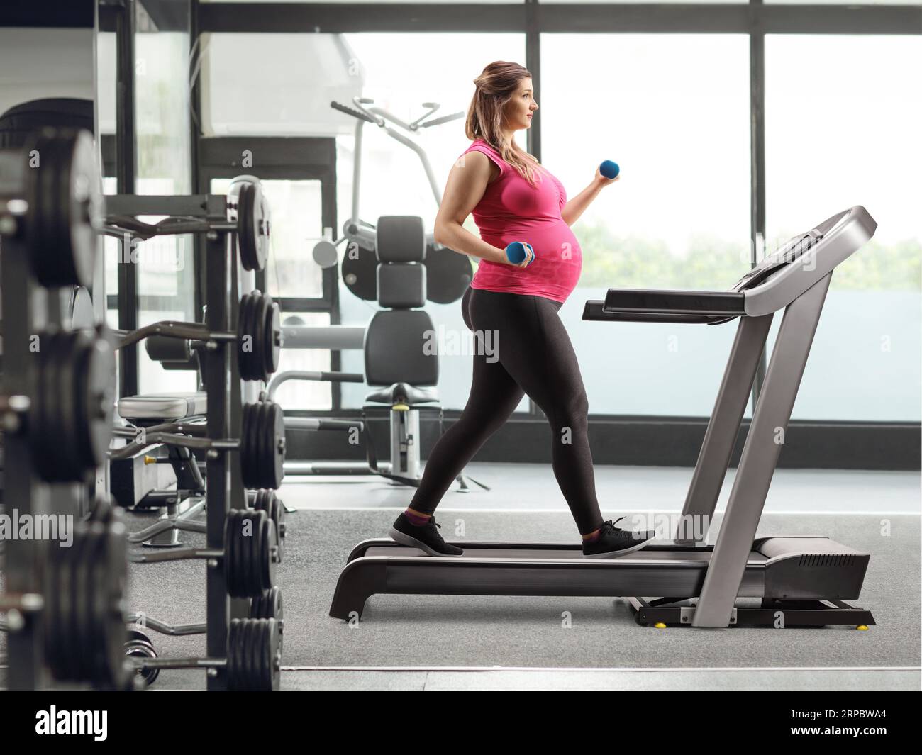 Full length profile shot of a pregnant woman walking on a treadmill with dumbbells in her hands at a gym Stock Photo Alamy
