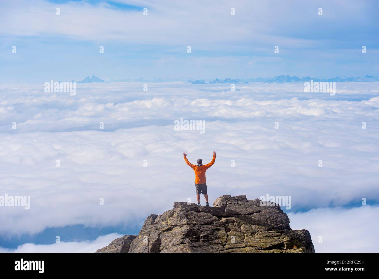 Man stretches arms overhead, mountain summit Stock Photo