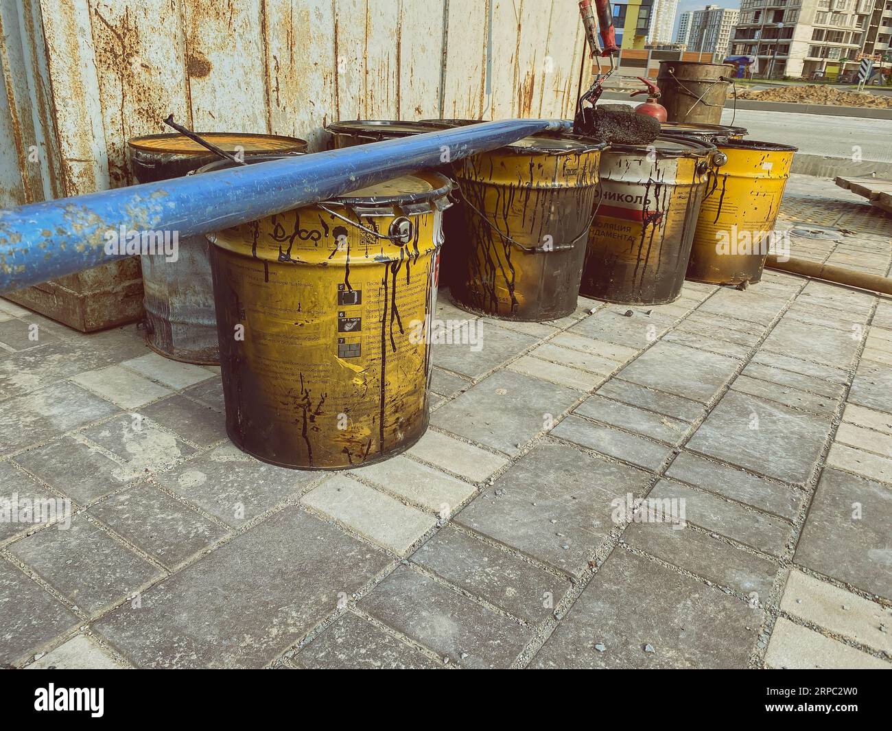 construction site. on the ground are barrels with building materials. black, viscous resin is spilled from the barrel. on the barrels lies a blue heav Stock Photo