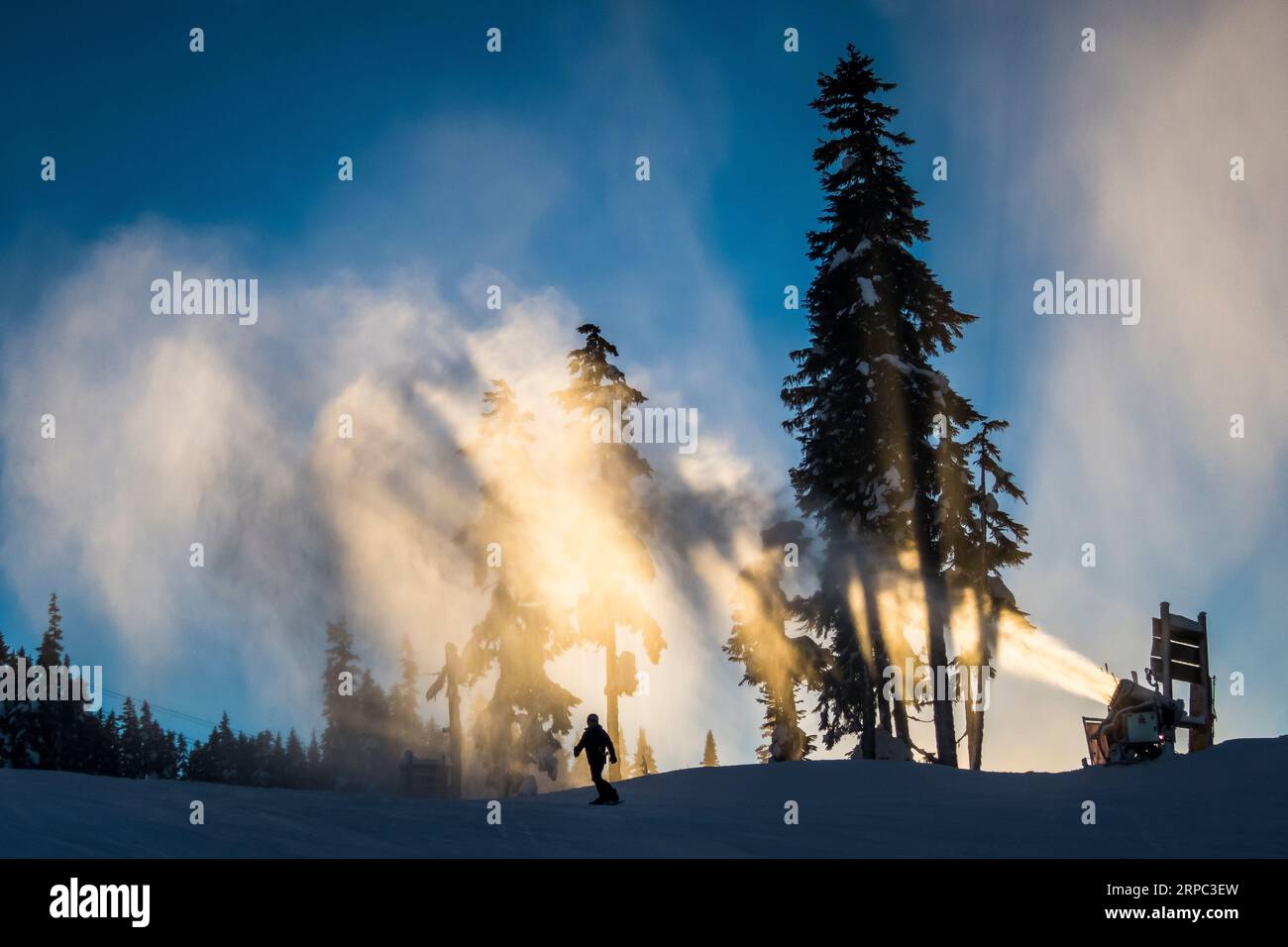 A Snow Gun Makes Snow As A Snowboarder Rides By At Whistler Blackcomb Ski Resort Stock Photo