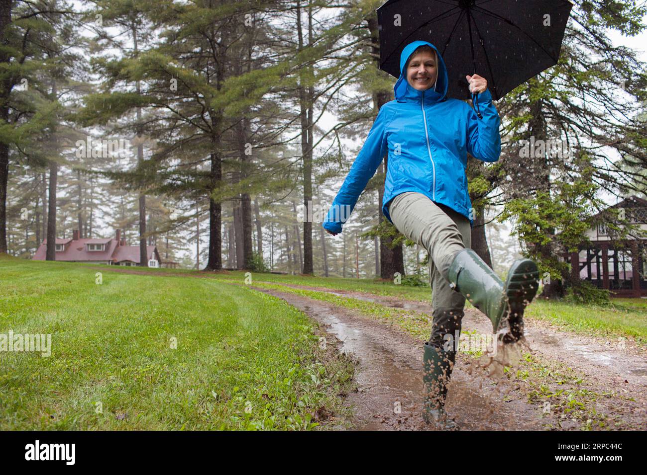 Middle-aged healthy woman happily splashes through puddles outside her cabin, in Kezar Lake, Maine Stock Photo