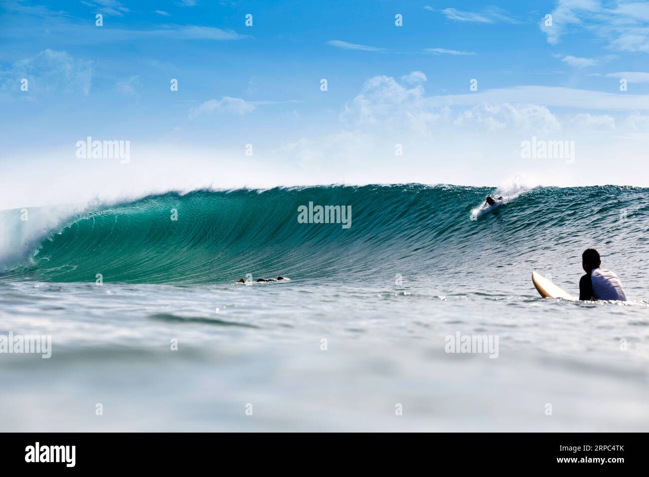 A Surfer looks on as another surfer rides a wave Stock Photo
