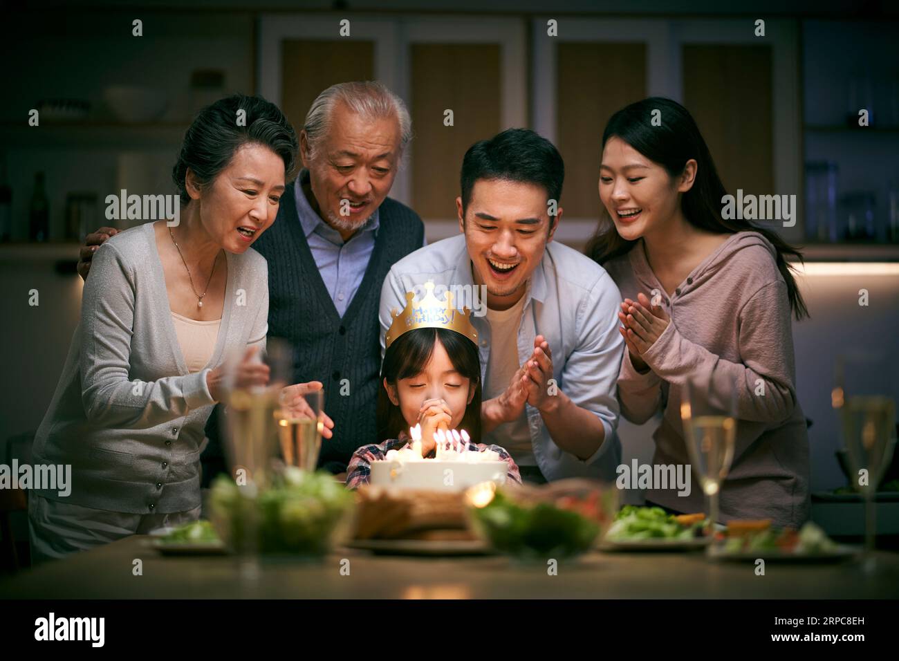little asian girl making a wish while three generation family