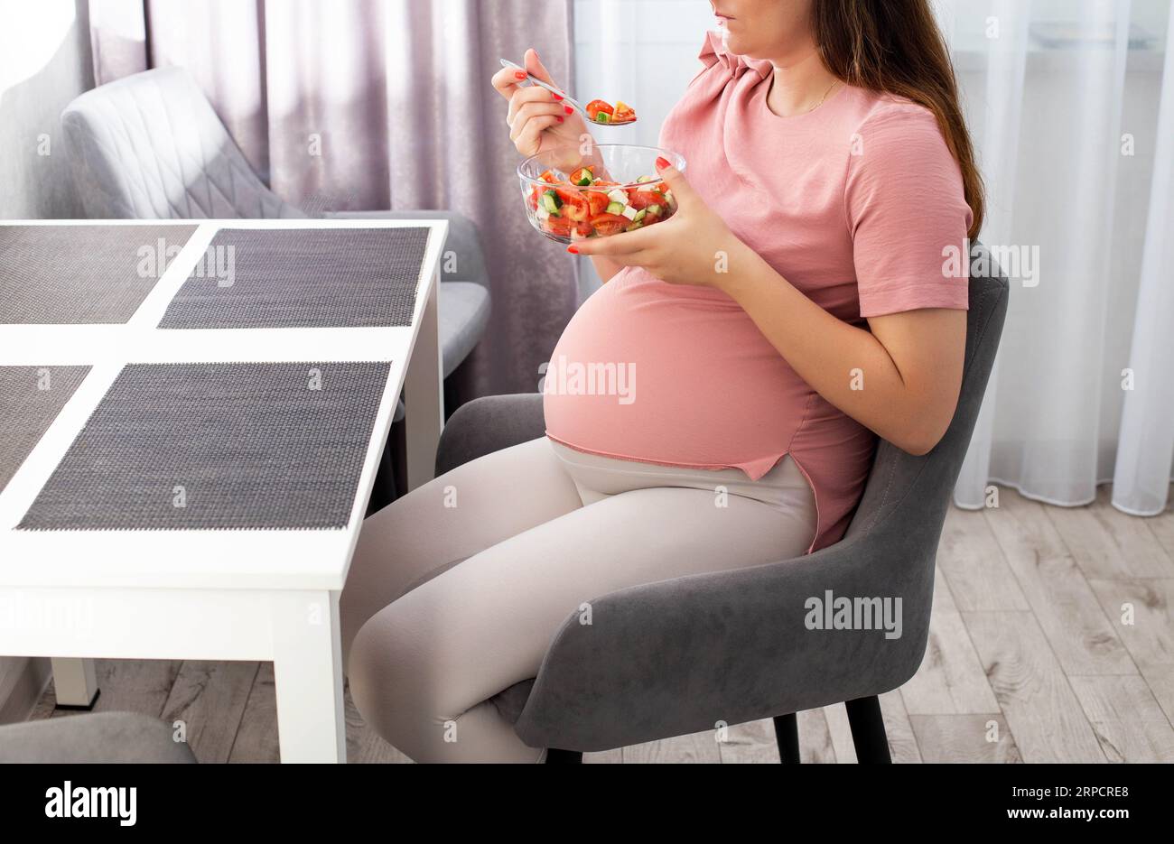 Pregnant girl eats vegetable salad in the kitchen. The concept of