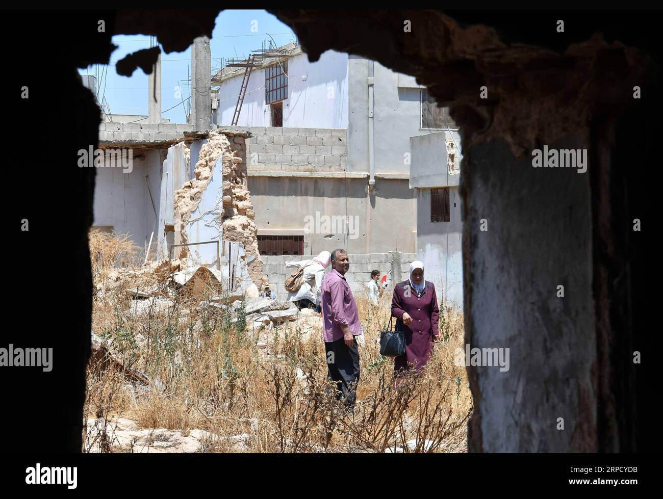 (190716) -- AL-QUSAYR, July 16, 2019 -- Wael al-Masri (L), 48, stands with his cousin Hafiza Masri at the gate of the family s shattered home upon returning to the town of Al-Qusayr in the central Syrian province of Homs on July 7, 2019. In 2013, the Syrian army recaptured Al-Qusayr with the help of the Lebanese Hezbollah group, but the return of civilians had been suspended until the rebels threats were eliminated from nearby areas. Hundreds of happy returnees were overwhelmed in nostalgic feelings during the journey back home in a green bus provided by the government. But they were saddened Stock Photo