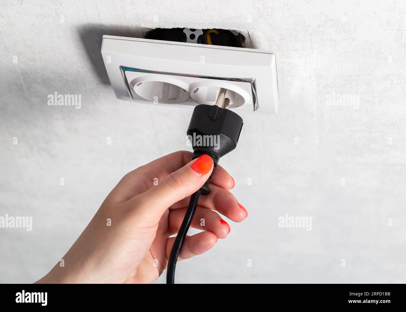 The girl puts the electric plug into a broken socket. Risk of electric