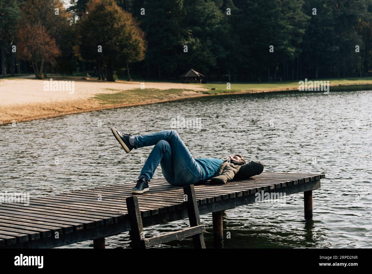A man lies with his leg behind his leg on a wooden pier on a lake in autumn Stock Photo