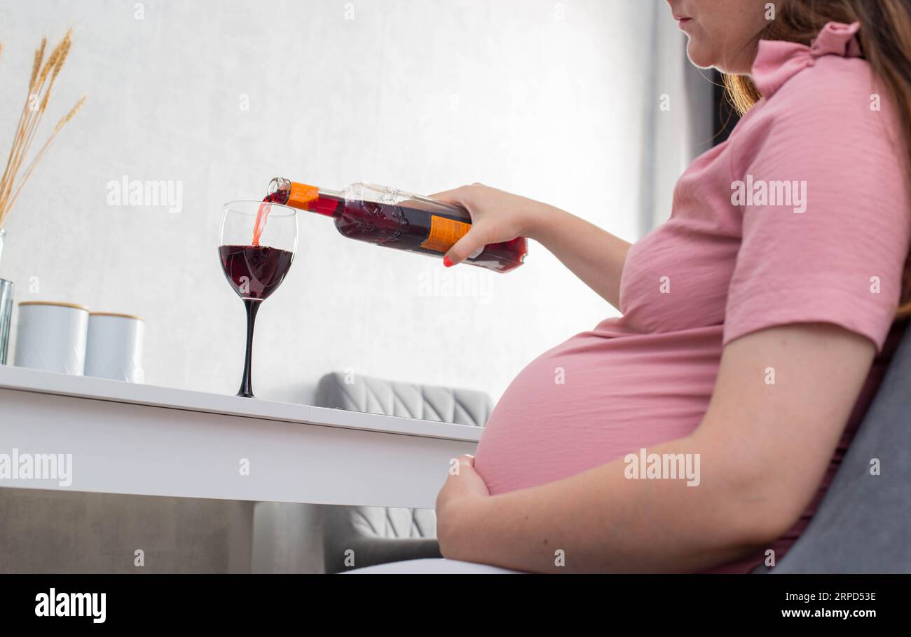 A pregnant girl pours wine from a bottle into a glass. The concept of drinking alcohol during pregnancy. Harm and cognitive impairment in a child. Alc Stock Photo