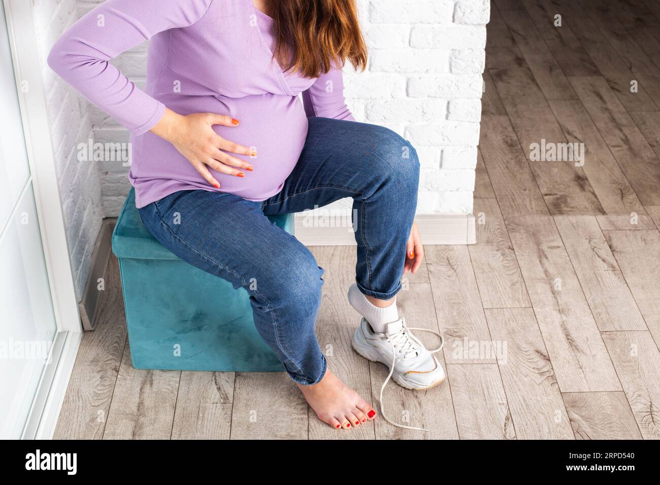 A pregnant girl puts on shoes with a big belly. and