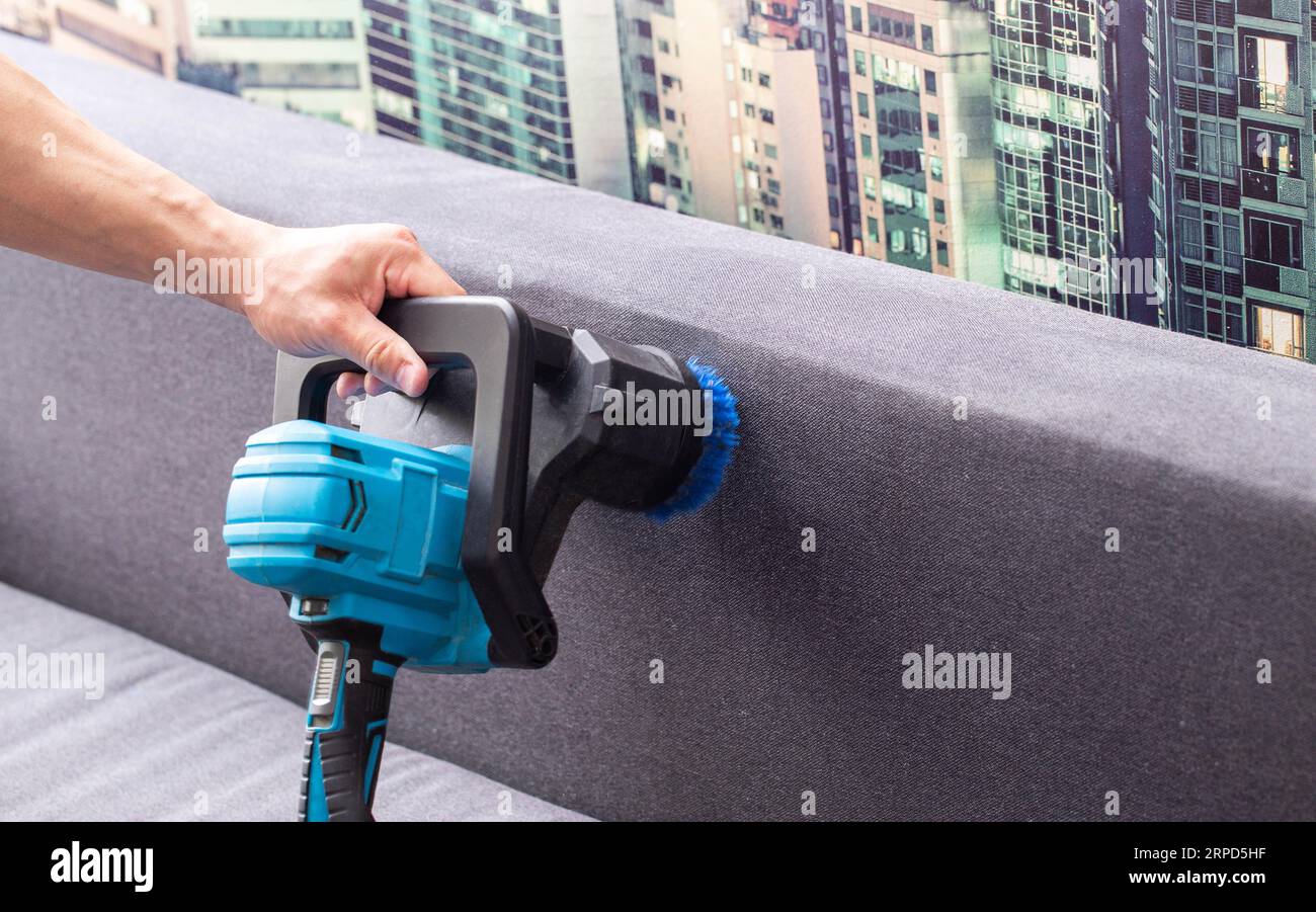 Cleaning the back of a black sofa with a special electric brush. Sofa