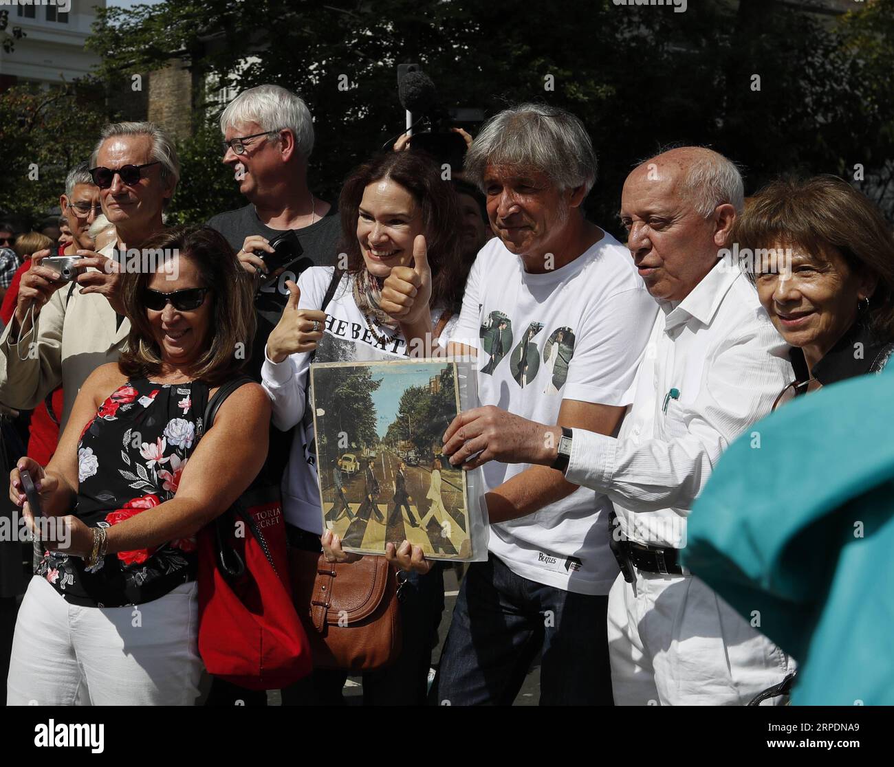 (190808) -- LONDON, Aug. 8, 2019 -- Beatles fans pose for photos with an original copy of the album cover of Abbey Road in London, Britain, Aug. 8, 2019. Exactly 50 years ago, Beatles members John Lennon, Paul McCartney, George Harrison and Ringo Starr walked on the zebra crossing outside their recording studio in north London to get the cover shot for the album Abbey Road . ) BRITAIN-LONDON-BEATLES-ABBEY ROAD-PHOTOGRAPH HanxYan PUBLICATIONxNOTxINxCHN Stock Photo