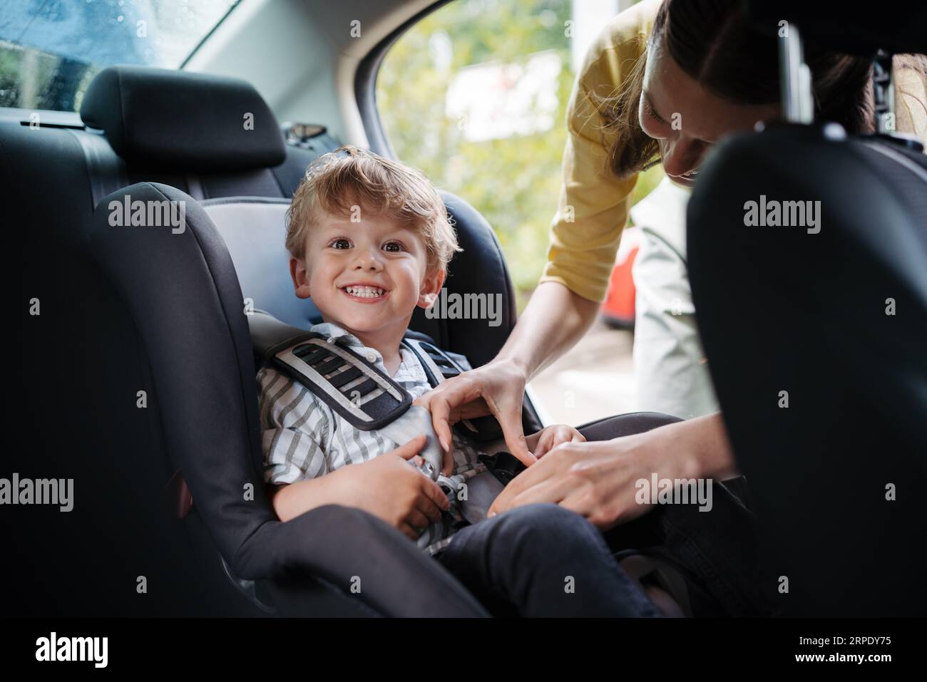 Young mother putting her little son in car seat. Stock Photo